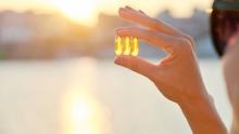 Bir kadın, güneşin önünde vitamin kapsülleri tutuyor.