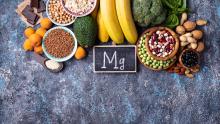 Besinlerin besin değerleri sembolü olan "Mg" yazısı koyu bir arka plan üzerinde. Etrafında muz, ceviz, brokoli gibi besinler bulunuyor 