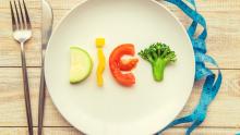 Masa üzerindeki tabak içerisinde sebzelerle "diyet" yazısı. Tabak yanında çatal, bıçak ve mezura bulunuyor.