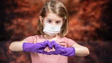  Bir tıbbi maske ve eldiven takan küçük bir kız çocuğu.