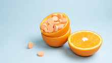  Turkuaz bir arka planda yer alan turuncu portakal kabuğu içerisinde tabletler ve yarım portakal