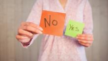 bir kadının bir elinde üzerinde NO yazan turuncu bir kağıt, diğer elinde YES yazan yeliş bir kağıt tutuyor