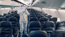 Betaz steril elbise, yüz maskesi ve eldiven takan kişi, uçak içindeki yolcu oturma alanını dezenfekte ediyor